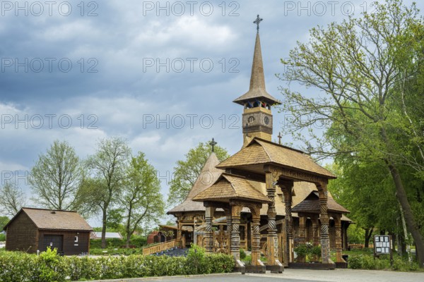 Impressive wooden church with elaborate wood carvings, surrounded by trees under a cloudy sky, The
