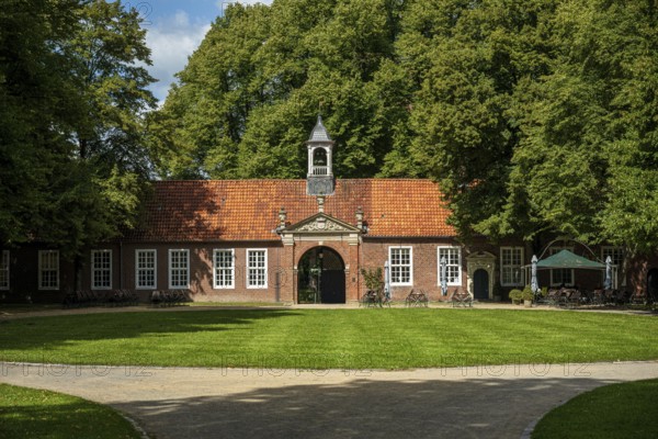 A brick building with a bell tower in front of a grassy area and surrounded by tall trees in the