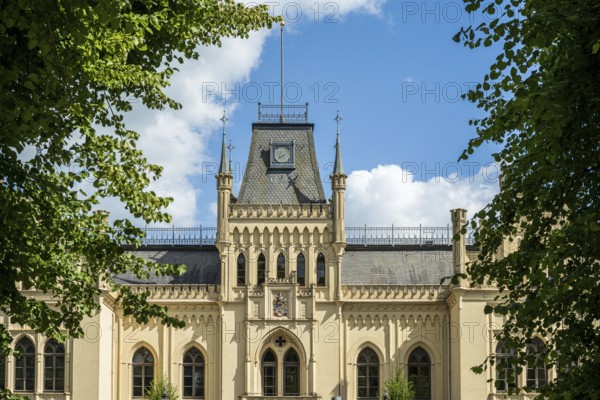 A Gothic castle with towers surrounded by green trees under a blue sky, Schloss Evenburg, Leer,