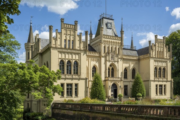 A magnificent Gothic-style castle surrounded by green trees and blossoming nature, Schloss