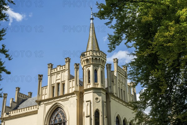 The Gothic-style castle tower rises into the blue sky, surrounded by trees, Schloss Evenburg, Leer,