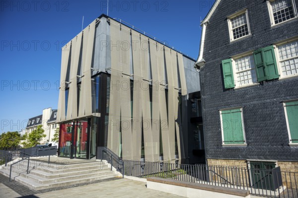 Modern building with a striking façade and large glass windows next to a traditional house under a