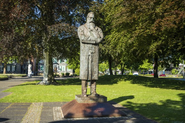 Statue of a man with crossed arms in a bright green park with trees in the background, statue of
