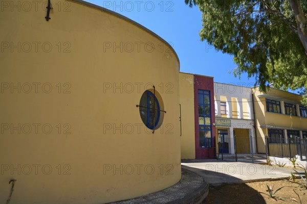Gymnasium, Yellow modern building with round shapes, next to a tree under a blue sky, Historicism,