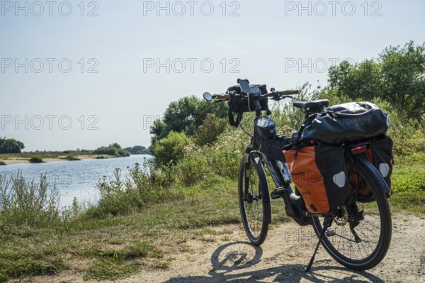 A bike with panniers stands on a sunny riverbank, embedded in nature, Weser cycle path, Weser,