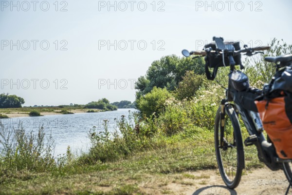 A bicycle stands on the riverbank, surrounded by a green landscape under a clear sky, Weser cycle