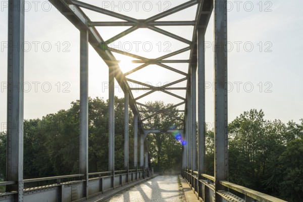 Metal bridge with sunlight, surrounded by trees, shows modern style, Weser cycle path, district of