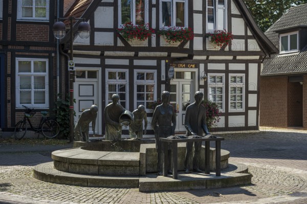Sculptures at a fountain in front of a traditional half-timbered house in a quiet city street,
