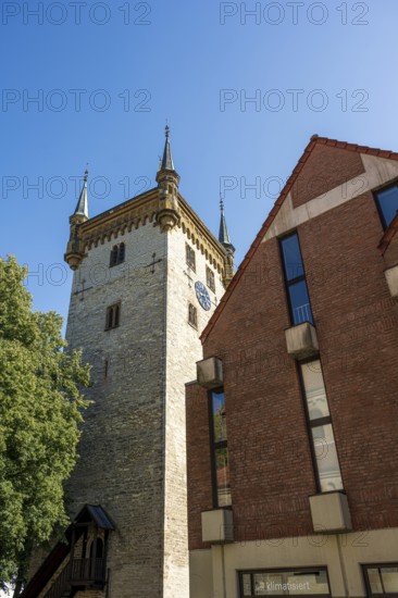 Historic tower and modern building, surrounded by trees, under a blue sky, tower of the old St