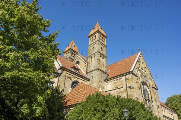 Gothic church with red tiled roofs, surrounded by green trees under a blue sky, St. Mary's Church