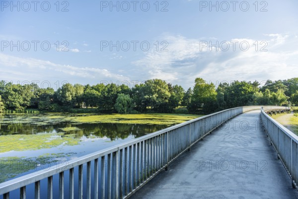 Bridge over a quiet river, surrounded by green trees and blue sky with clouds, Emssee near
