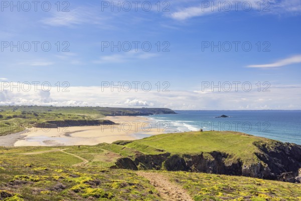 Sunny seascape view in a coastal landscape with a sandy beach and a rocky coastline from a meadow,