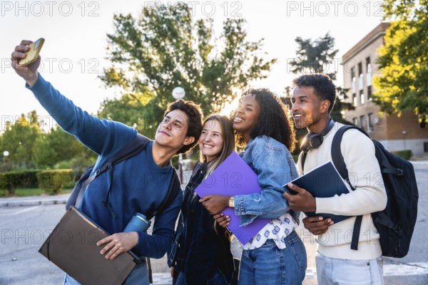 Diverse group of smiling university students recording a selfie outdoors on campus, holding books