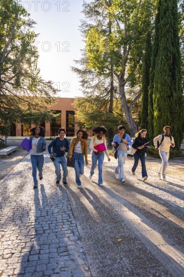 Group of diverse university students hurrying with textbooks and backpacks on a cobblestone path,