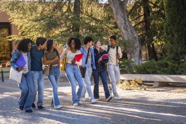 Group of multicultural university students walking and talking cheerfully together, carrying books,