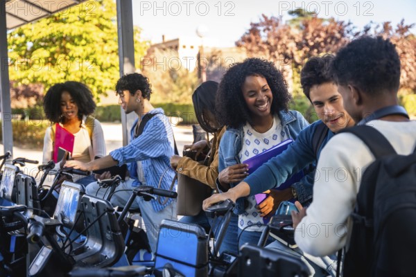 Group of happy diverse university students activating a shared bicycle from a station, preparing to