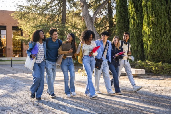 Diverse group of happy young university students walking together on campus, carrying books and