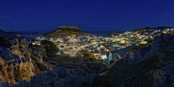 View of the illuminated town of Lindos with the ancient Acropolis under a starry sky with the sea,
