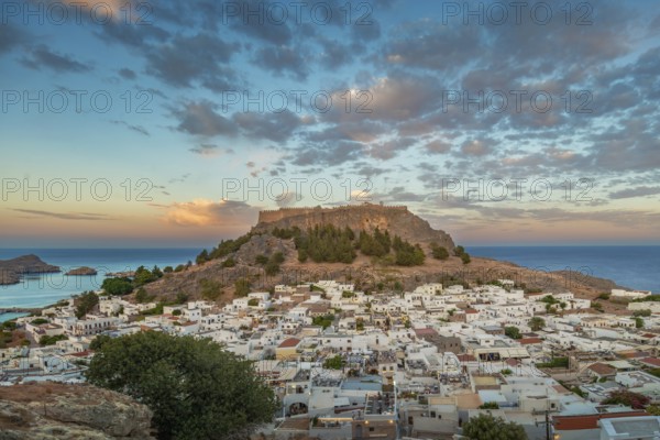 View of picturesque Lindos with the ancient Acropolis on a hill surrounded by the sea at sunset,