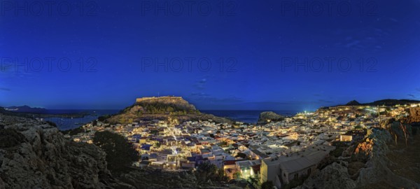 Wide angle photo of the city of Lindos with the ancient Acropolis in a clear night sky with glowing