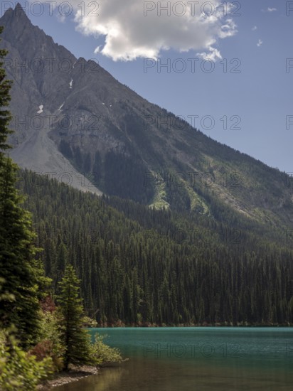 Steep mountain range of the Canadian Rocky Mountains above dense forest and Emerald Lake inside