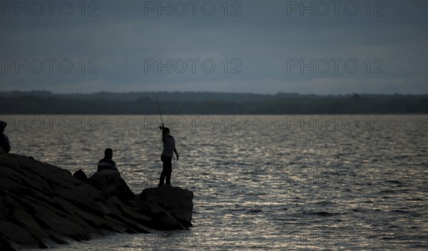 A person fishing on a rocky shore at dusk with a calm lake in Ottawa, Ontario, Canada, North
