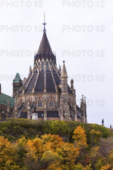 A Gothic-style Canadian Parliament building with a prominent spire, surrounded by colorful autumn