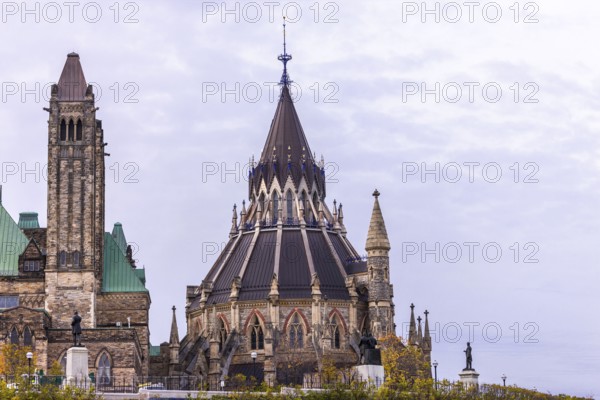 The Canadian Parliament Buildings with an ornate spire and towers against a cloudy sky, showcasing