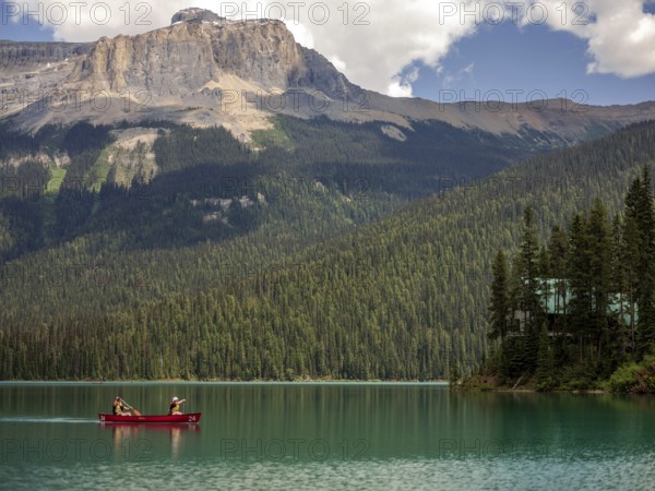 Canoe on Emerald Lake encircled by the Canadian Rocky Mountains and dense forest under a bright sky