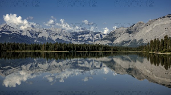 Majestic mountains of the Canadian Rocky Mountains and forest reflected in calm lake under a clear