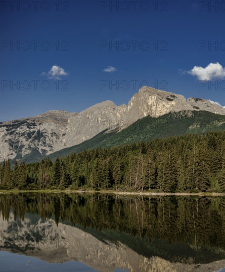 Tall mountains of the Canadian Rocky Mountains and trees reflecting in a serene lake under a clear