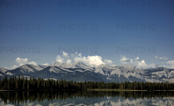 Majestic mountain range of the Canadian Rocky Mountains mirrored in a tranquil lake under a vast