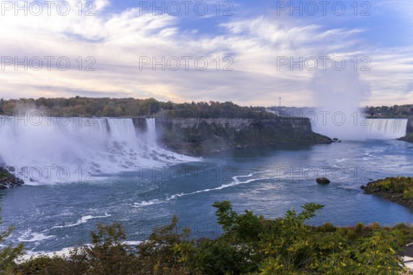 Wide view of the Bridal Veil Falls and the Horseshoe Falls with mist rising under a partly cloudy