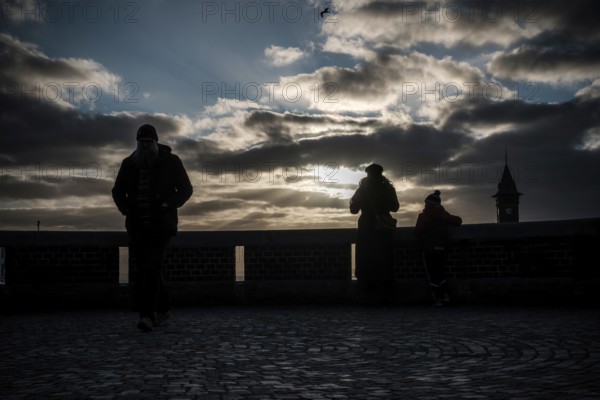Silhouetted figures at sunset with dramatic clouds and a distant tower in Helsingborg, Sweden,
