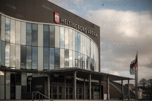 Helsingborg Arena featuring a glass facade, flags, and situated under cloudy weather in