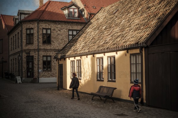 A quiet street with brick buildings and tile roofs, bathed in warm autumn light and shadows in