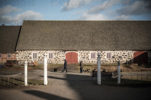 Stone building with red doors on a farm, people walking dogs in foreground in Helsingborg, Sweden,