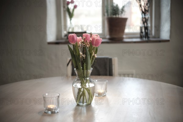 Close-up of a vase filled with tulips on a wooden table, with soft candle lights in Helsingborg,