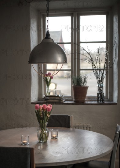 A cozy table setting with tulips and a soft glow from a pendant light, framed by a window in