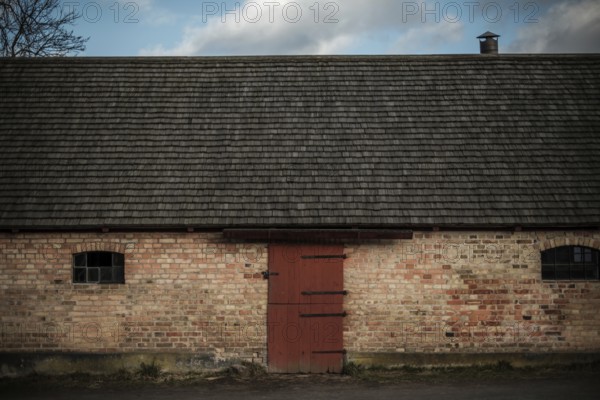A rustic brick building with a red door under an overcast sky, featuring a chimney in Helsingborg,