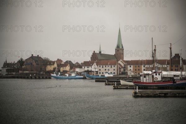 A harbor with docked boats and a church in the background on a cloudy day in Helsingor, Denmark,