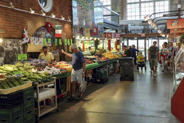 Indoor St. Lawrence Market scene with people browsing stalls filled with colorful produce in