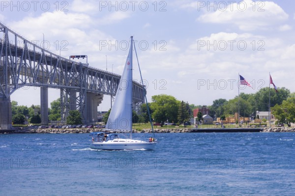 Sailboat gliding near the Blue Water Bridge, connecting Canada and the United States, with flags
