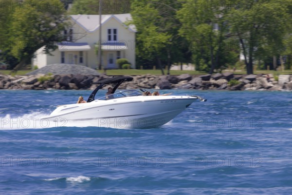 A speedboat glides quickly across the water with trees and houses in the background along the St.
