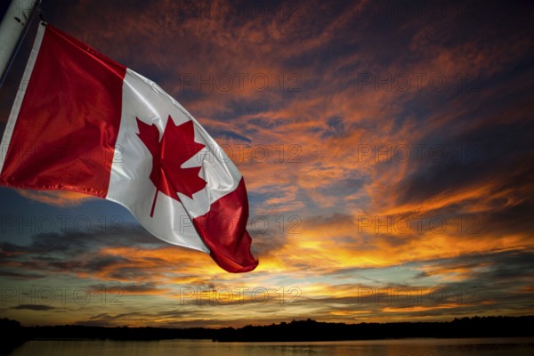 The Canadian flag waves against a vibrant sunset sky filled with colorful clouds in Muskoka,