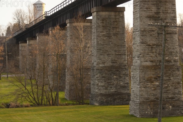 Image of a stone bridge structure with green grass and trees, highlighted by warm tones in St.
