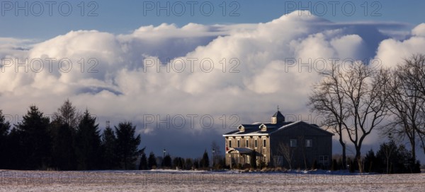Color image of a house with large clouds in the background, set in a tranquil winter landscape in