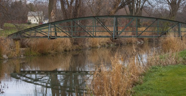 Rustic bridge over a creek with reflections, surrounded by autumn trees and grass, creating a