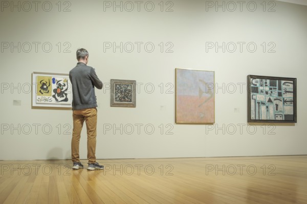 Jan 13, 2024 - Lisbon, Portugal: visitor in gray jacket and tan pants observe abstract artworks