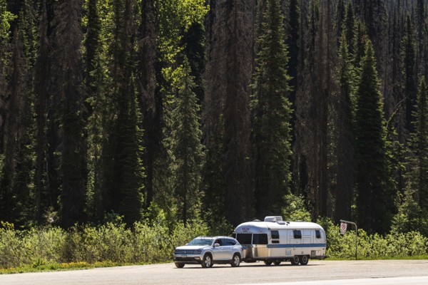 An Airstream travel trailer parked with a car by a dense forest, highlighting travel adventure in